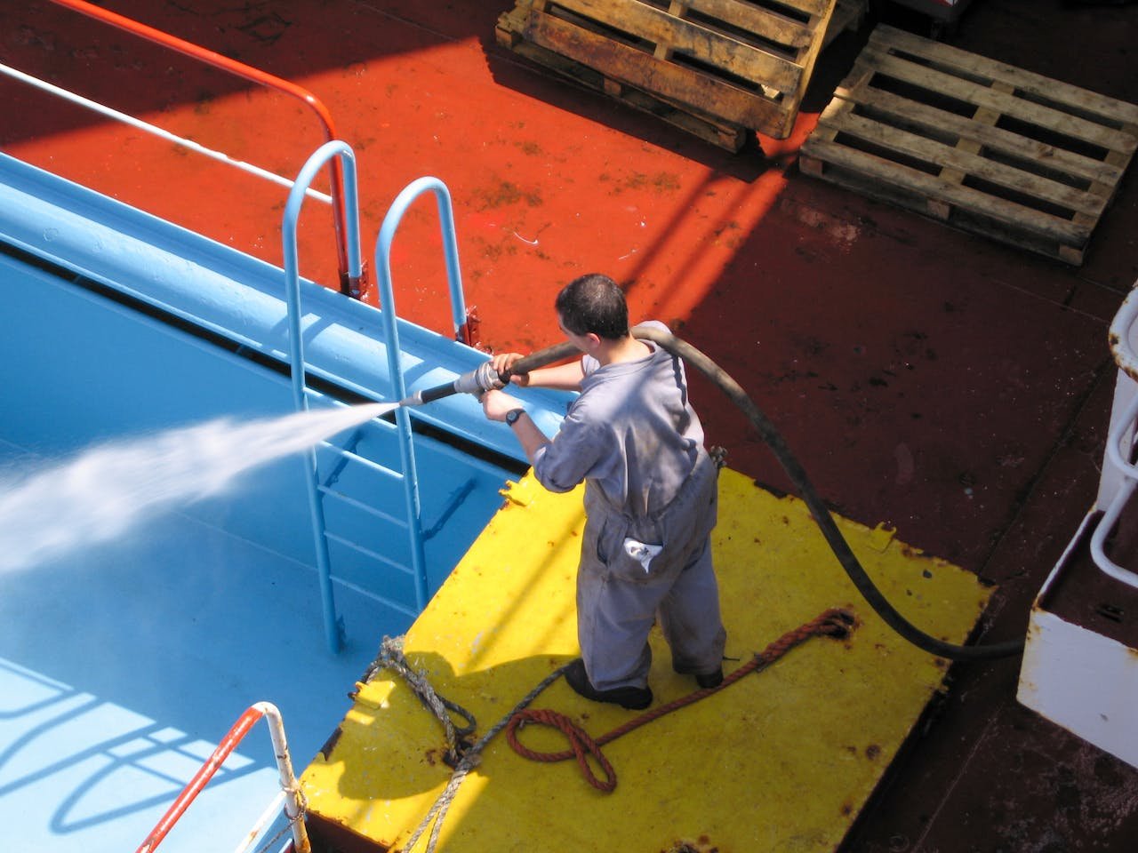 The Art of Drawing Readers In: Your attractive post title goes here A worker using a high-pressure hose to clean the deck of a ship, showing industrial processes.