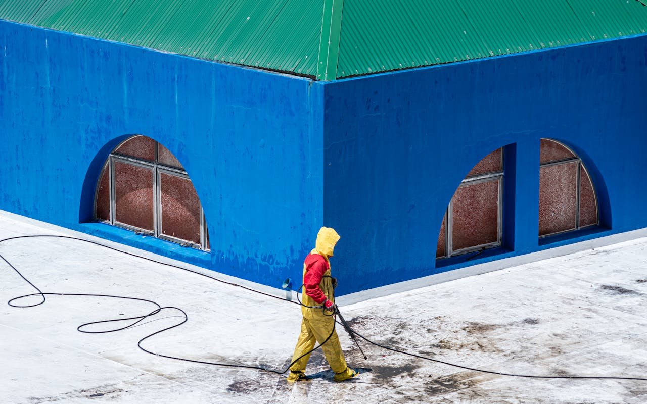 Mastering the First Impression: Your intriguing post title goes here A worker in protective gear power washes a vibrant blue building exterior.